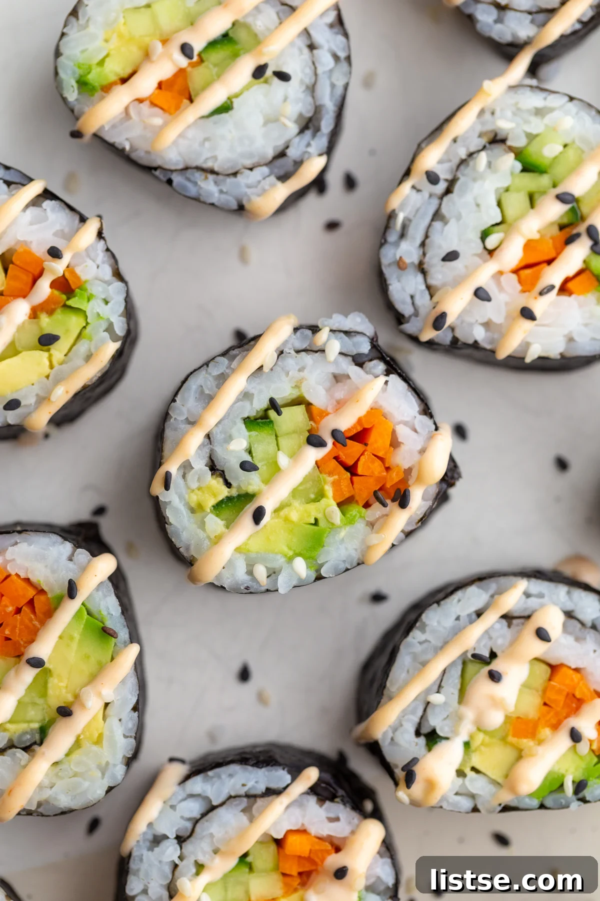 A perfectly prepared cucumber roll, showcasing creamy avocado and vibrant pickled carrot, elegantly drizzled with spicy mayo.