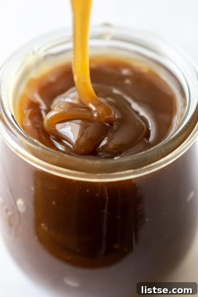 A small glass jar overflowing with creamy caramel sauce, ready to be enjoyed.