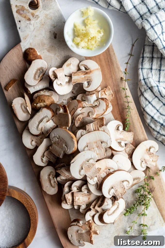 Freshly sliced cremini mushrooms arranged on a rustic wooden cutting board, ready for cooking.