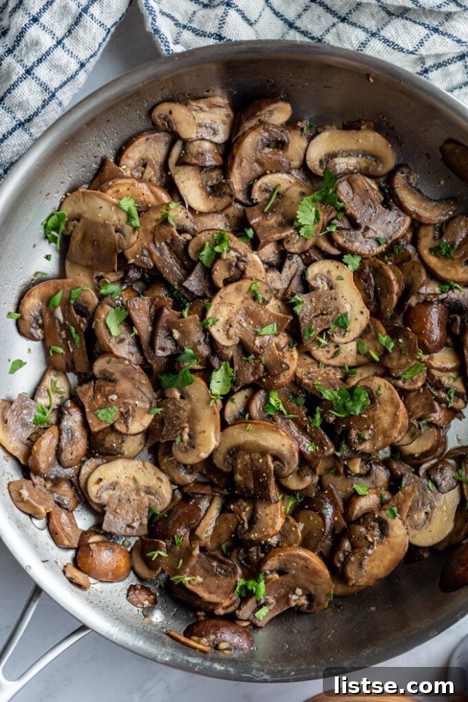 Close-up of cremini mushrooms beautifully sautéing in a large, hot skillet, turning golden brown.
