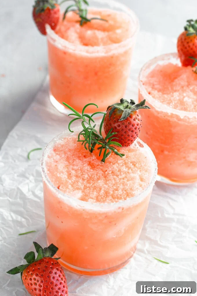 A frosty glass of Frozen Strawberry Salty Dog cocktail garnished with fresh strawberries and rosemary, perfect for summer.