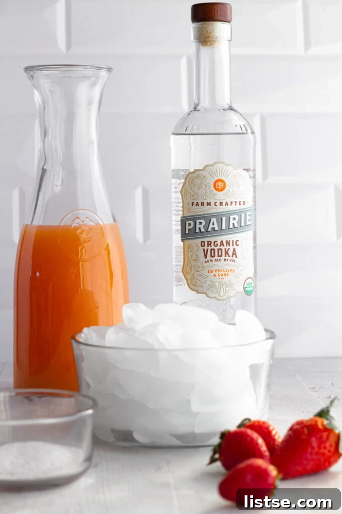 Ice in a bowl with bottles of grapefruit juice and vodka in the background, showing the primary ingredients for the cocktail.