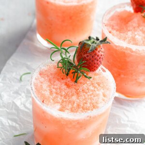 Small glass with a frozen salty dog slushie with fresh strawberries and rosemary on top, ready for serving.