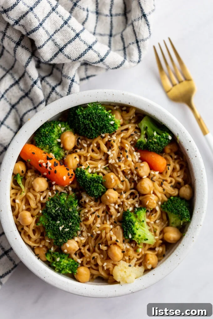 A beautifully presented bowl of elevated ramen, rich with vegetables and sesame seeds, resting on a textured surface with a soft towel in the background.