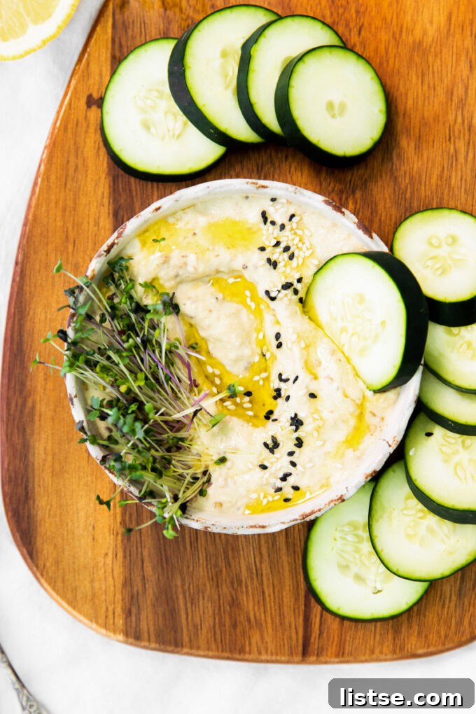 Creamy Baba Ganoush dip served in a rustic bowl with a slice of fresh cucumber dipped in, surrounded by more vegetables and pita bread