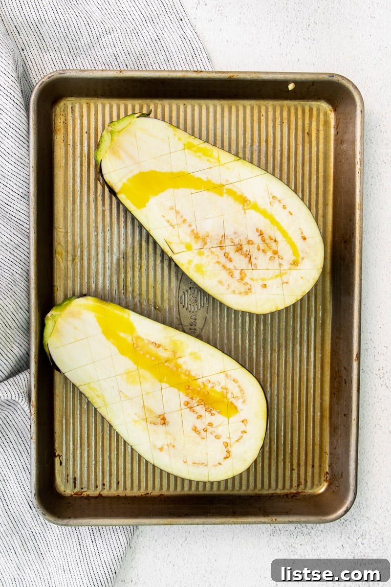 Eggplant halves seasoned with olive oil on a parchment-lined baking sheet, ready for roasting