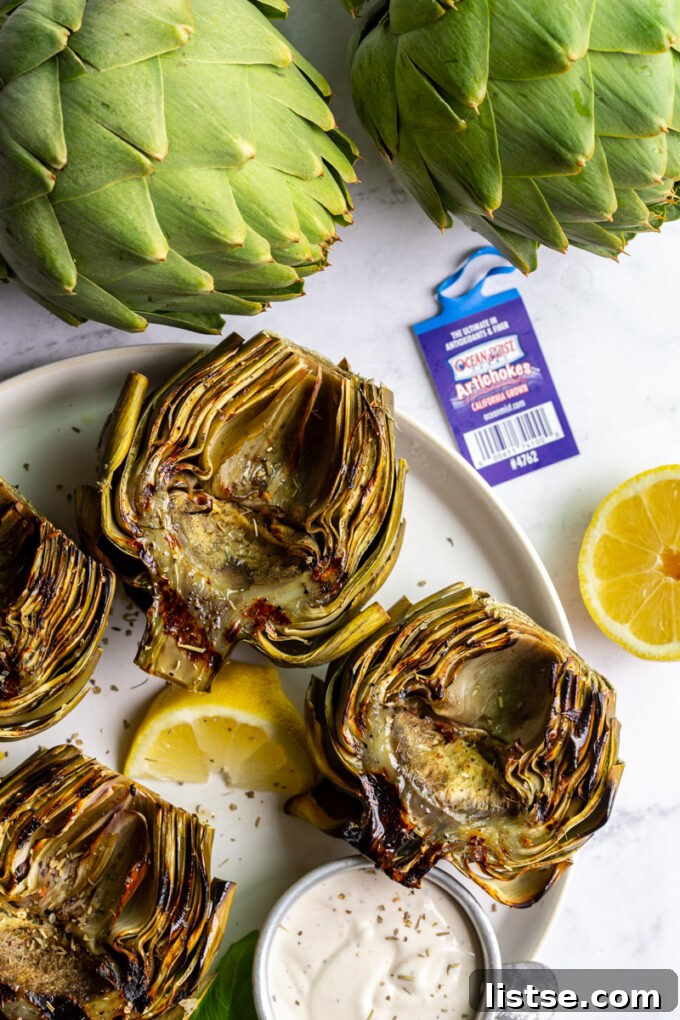 Fire-Kissed Artichokes 3 A large platter holds four grilled artichokes and lemon slices, with fresh, raw artichokes visible in the background.