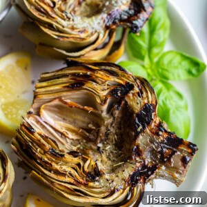 Fire-Kissed Artichokes 7 Grilled artichokes on a plate with lemon wedges.