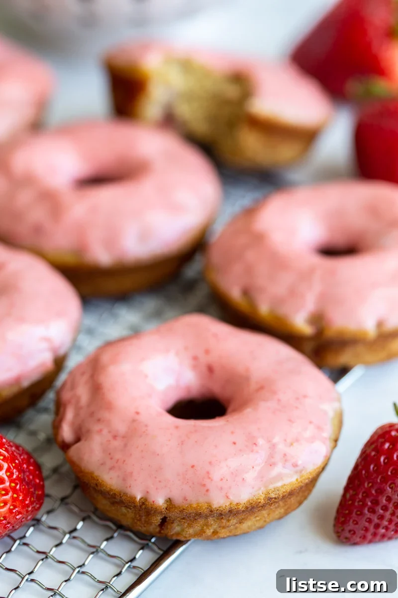 Freshly baked vegan strawberry donuts topped with a luscious pink strawberry glaze, arranged on a cooling rack.