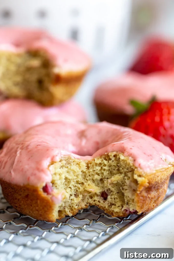 Close-up of a vegan strawberry donut with a bite taken out, showcasing the pink glaze and soft interior.