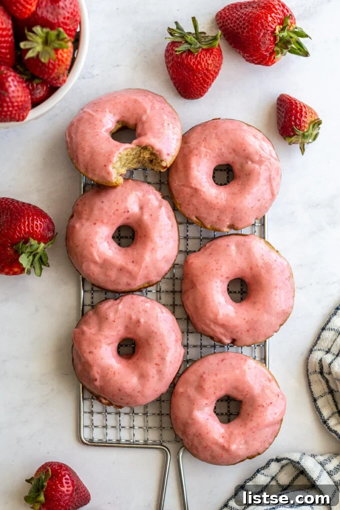 Close-up of baked strawberry glazed donuts on a wire cooling rack, surrounded by fresh strawberries.