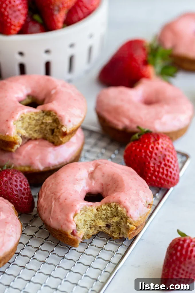 A beautifully arranged plate of freshly baked vegan strawberry donuts, some with a bite taken, showing the perfect texture and vibrant glaze.