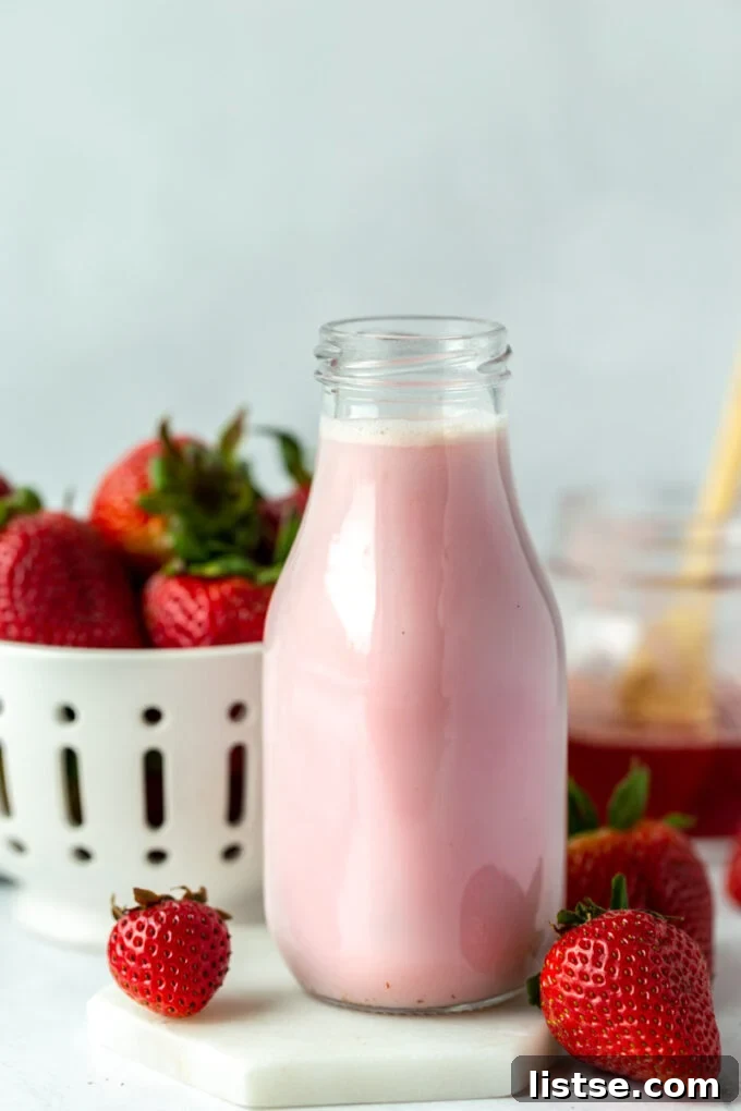 Homemade strawberry milk in a glass jar, garnished with fresh strawberries on the side