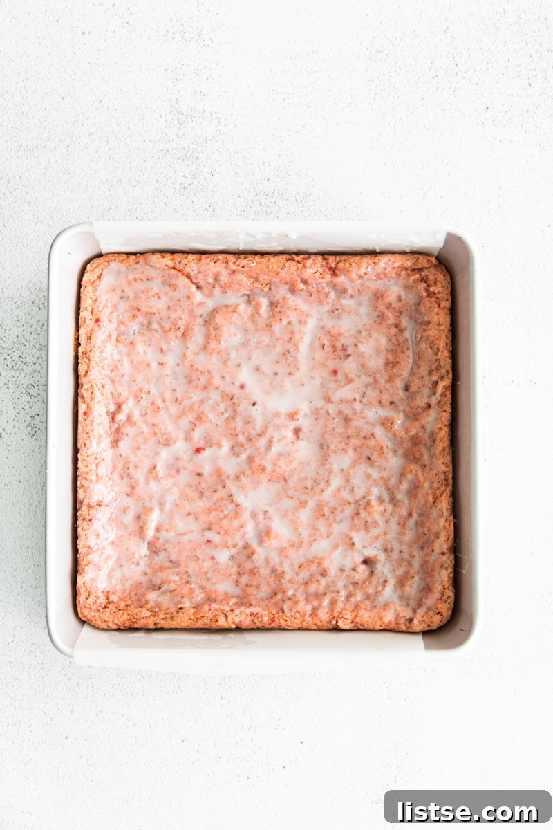 Strawberry Chocolate Bliss 8 Baked pink brownies with a vanilla glaze in a small baking pan, cooling.