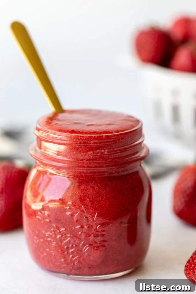A small glass jar brimming with homemade strawberry puree, with a spoon resting inside, ready to be enjoyed.