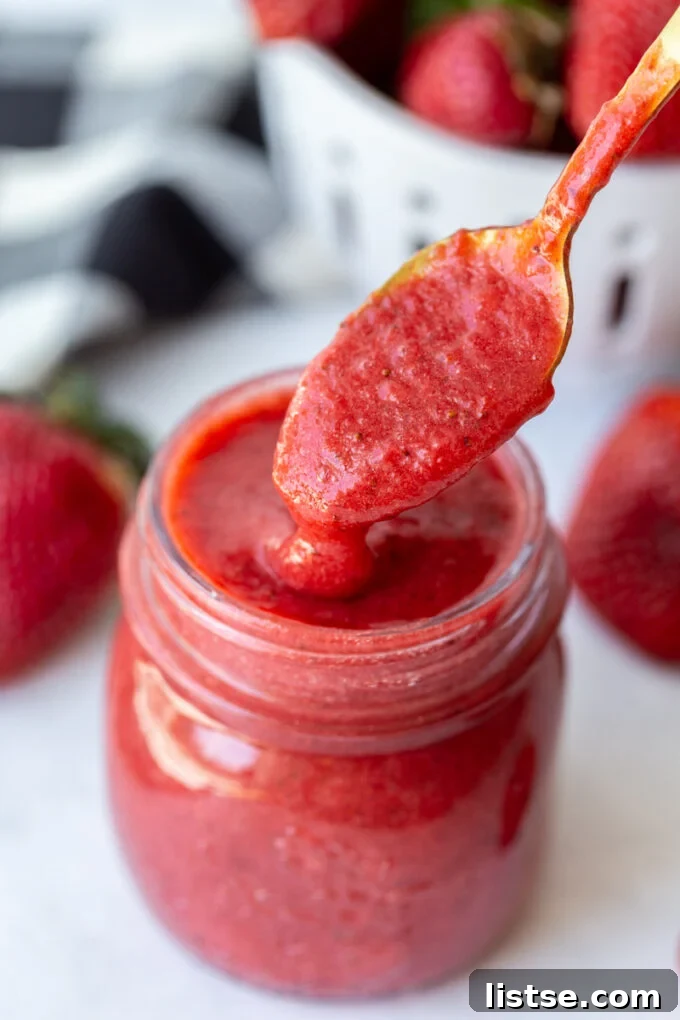A person expertly spooning thick, glossy strawberry puree into a glass jar, highlighting its rich texture and ease of transfer.