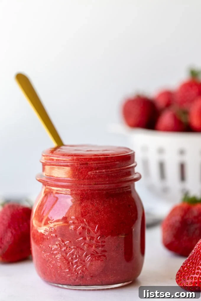 A beautifully presented small glass jar of strawberry puree, with a spoon nestled within, ready to be served or stored.
