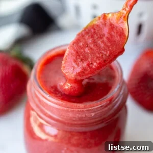 Homemade strawberry puree being spooned out of a jar, ready to be served.