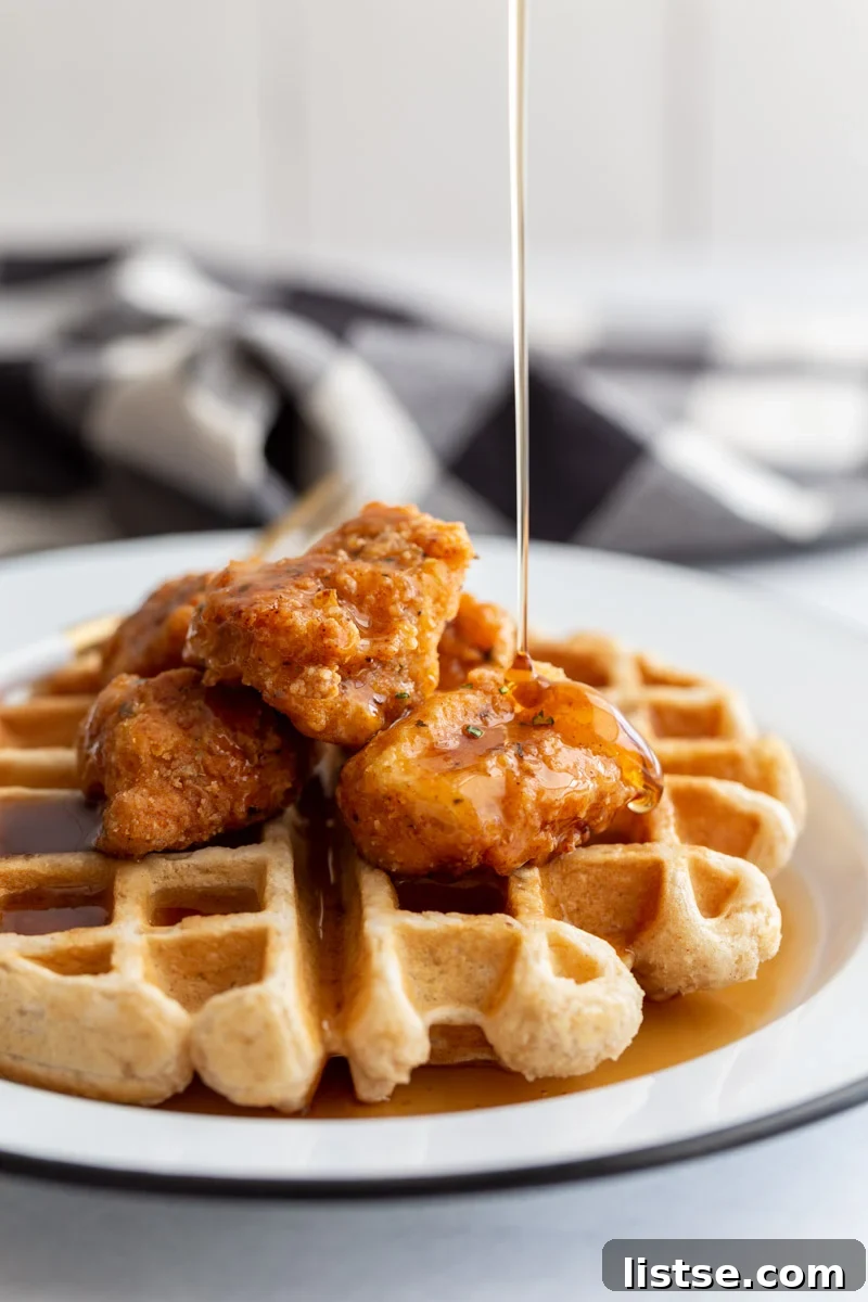 waffle on a white plate topped with vegan chicken nuggets and a drizzle of syrup pouring on top