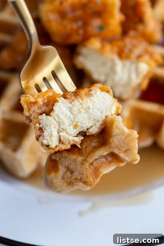 bite of vegan chicken and waffles on a fork with the rest of the dish behind in