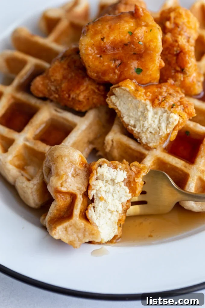 bite of vegan chicken and waffles on a fork with the rest of the dish behind in