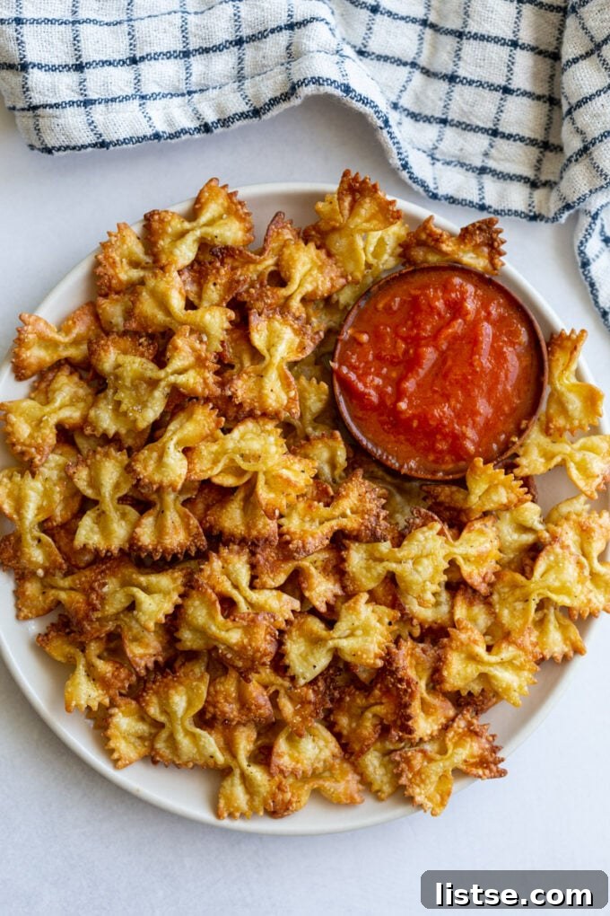 Crispy Pasta Bites 5 Delicious air fryer pasta chips on a white plate with a side of marinara sauce and fresh basil garnish