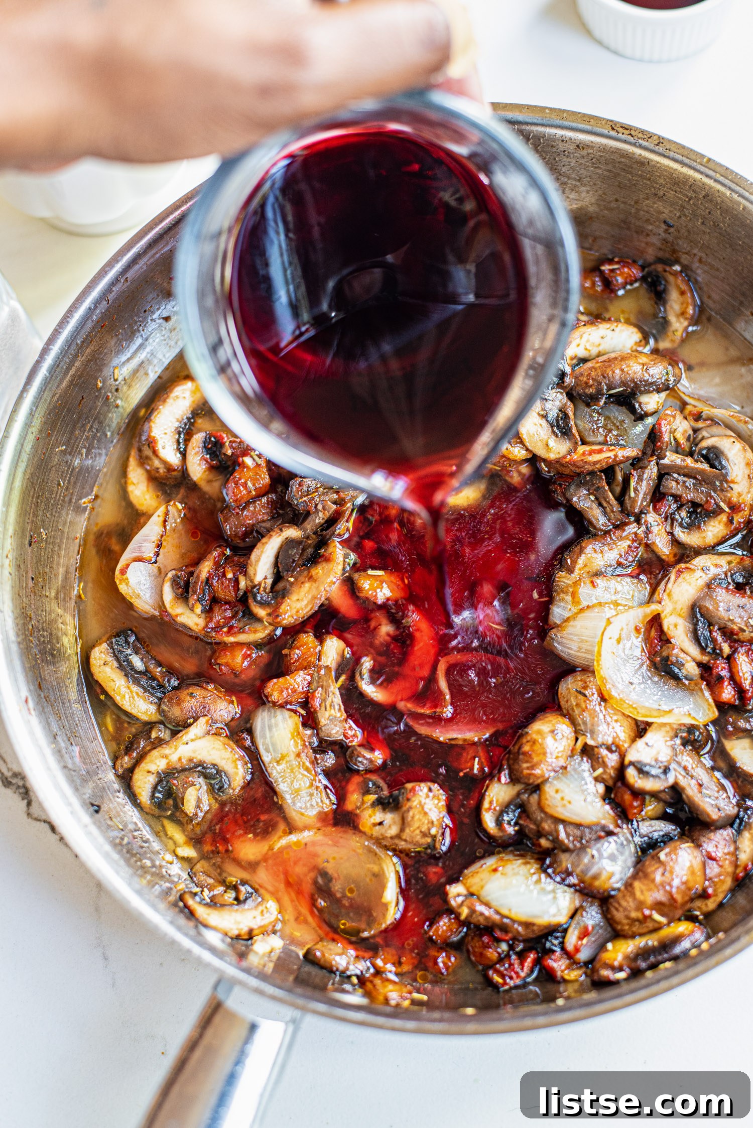 Pouring red wine over mushrooms in a skillet