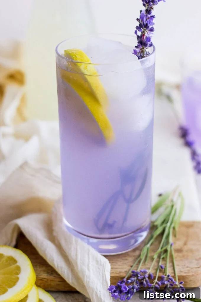 A tall glass filled with icy lavender lemonade, garnished with a lemon slice and a fresh lavender sprig, ready to be served.