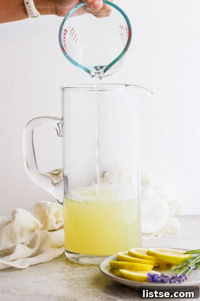 Lemon juice and water being poured and mixed together in a large glass pitcher.