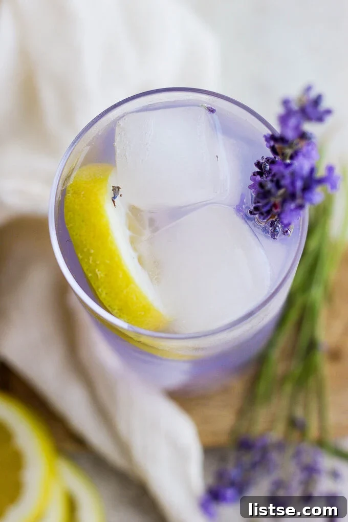 A close-up of a glass of lavender lemonade with ice, lemon slices, and a fresh lavender sprig, highlighting its refreshing qualities.