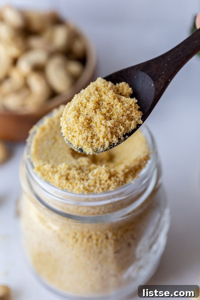 vegan parmesan cheese in a glass jar with cashews in the background. wood spoon scooping some up