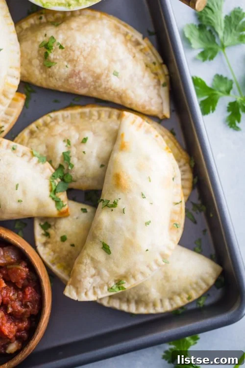 empanadas stacked up on a back tray with salsa in the corner