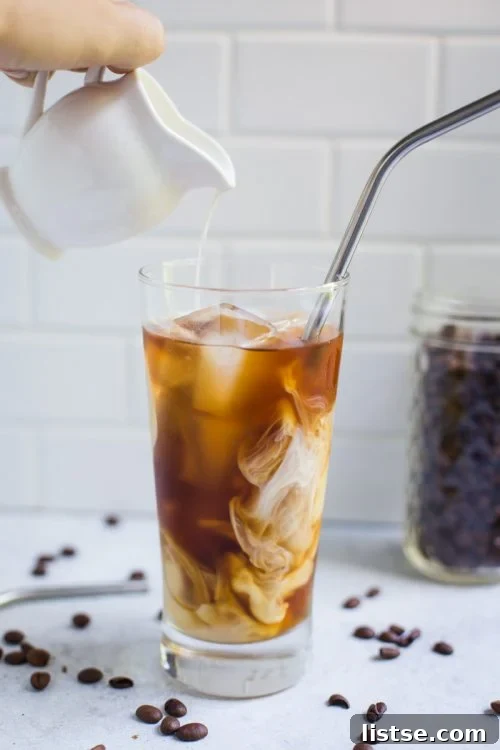 Culinary Delights Beginning with I 3 A refreshing glass of iced coffee, with cream being elegantly poured in, creating a beautiful swirl of light and dark brown.