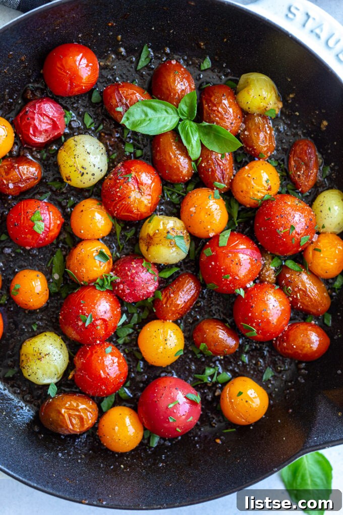 Close-up of cherry tomatoes gently sautéing in a cast iron skillet, with some beginning to blister.