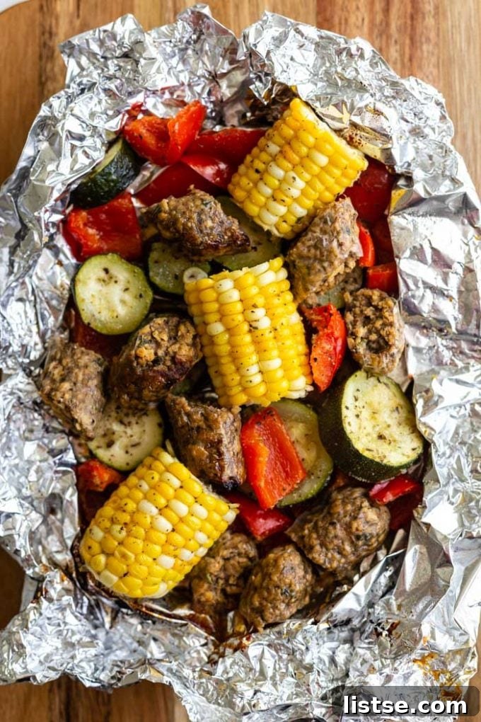 Grilled vegan sausage and colorful chopped bell peppers, onions, and zucchini cooking inside a foil pack, perfect for a campfire or oven.