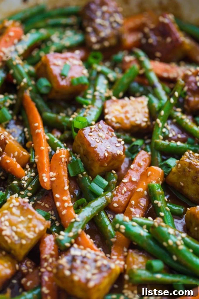 Plate of glazed sesame ginger tempeh with a sprinkle of green onions and sesame seeds.