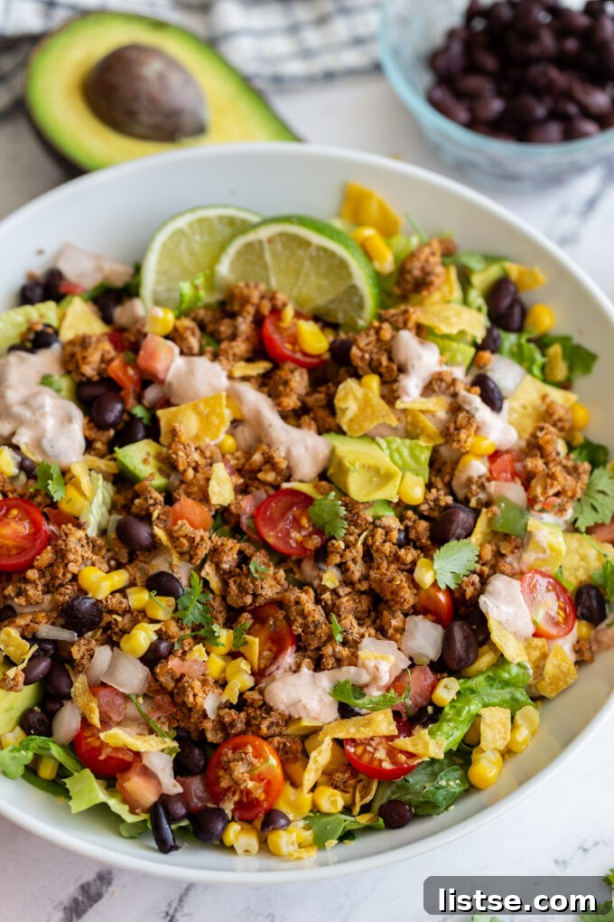 A beautifully presented vegetarian taco salad, generously topped with crisp lettuce, juicy tomatoes, creamy avocado slices, our homemade walnut meat, and a drizzle of cool, savory cream sauce.