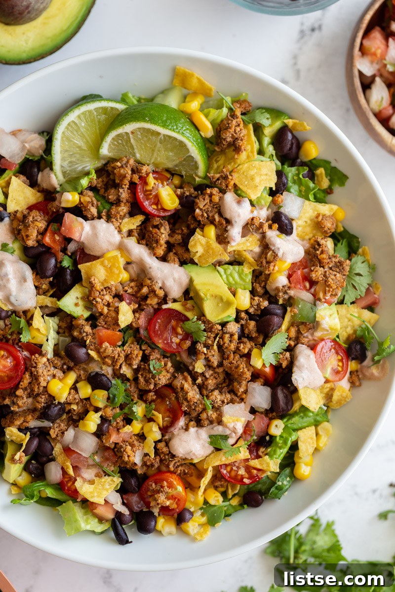 A vibrant and fresh vegetarian taco salad, generously layered with crisp lettuce, ripe tomatoes, creamy avocado, savory walnut meat, and a smooth cream sauce.