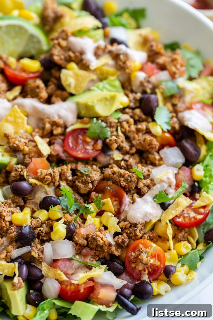 Close-up shot of a vegetarian taco salad showcasing vibrant ingredients like crisp lettuce, juicy tomatoes, creamy avocado, hearty walnut meat, and a generous drizzle of a creamy, tangy sauce.