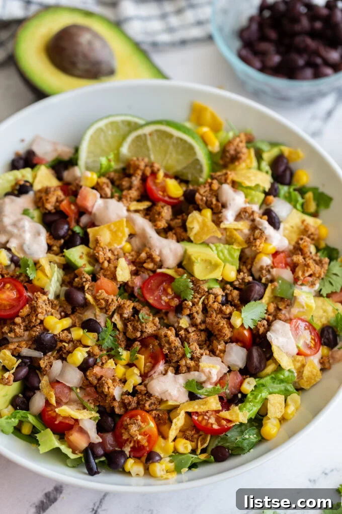 Appetizing vegetarian taco salad featuring crisp lettuce, diced tomatoes, sliced avocado, hearty walnut meat, and a rich, creamy sauce, garnished with a lime wedge.