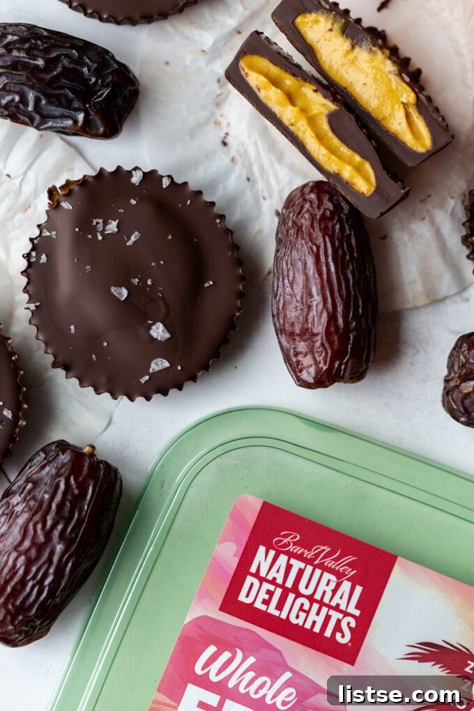 Date Sweet Pumpkin Peanut Butter Cups 3 Two pumpkin peanut butter cups, one cut in half revealing the creamy pumpkin and date filling, alongside a small basket of fresh Medjool dates.