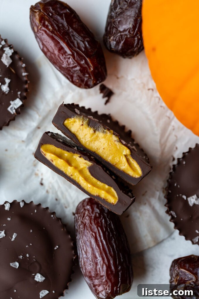 Date Sweet Pumpkin Peanut Butter Cups 4 A perfectly halved Date Sweetened Pumpkin Peanut Butter Cup, revealing its distinct layers of chocolate and the light orange pumpkin filling, with a decorative mini pumpkin in the background.