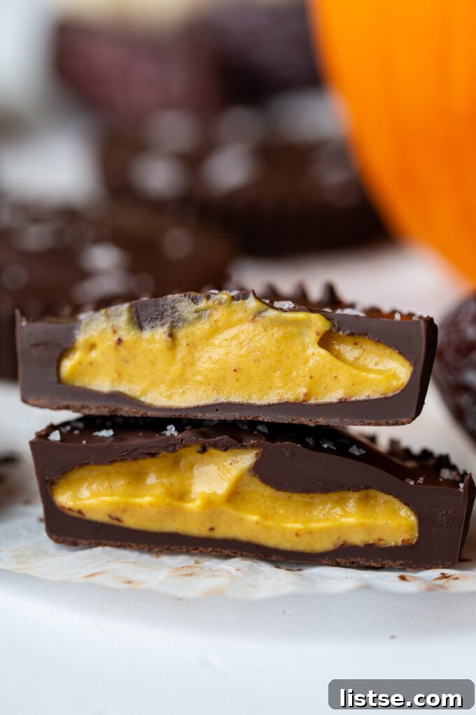 Date Sweet Pumpkin Peanut Butter Cups 5 A single Date Sweetened Pumpkin Peanut Butter Cup, perfectly sliced in half to showcase its delightful layers, placed next to a miniature decorative pumpkin.