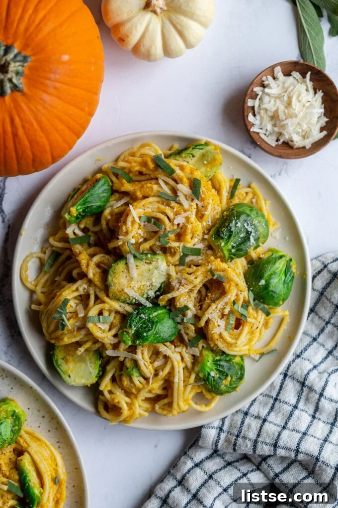 A delicious serving of creamy pumpkin pasta spaghetti on a plate, garnished with tender Brussels sprouts. Decorative small pumpkins are subtly positioned in the corner of the frame, adding to the autumnal feel.