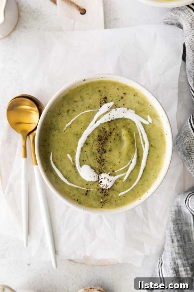 zucchini soup in a white bowl served with a gold and white spoon
