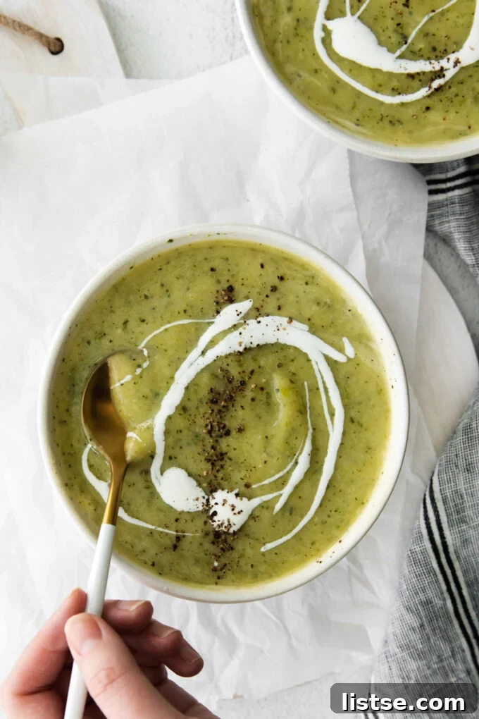 woman's hand stirring vegan zucchini soup with a spoon