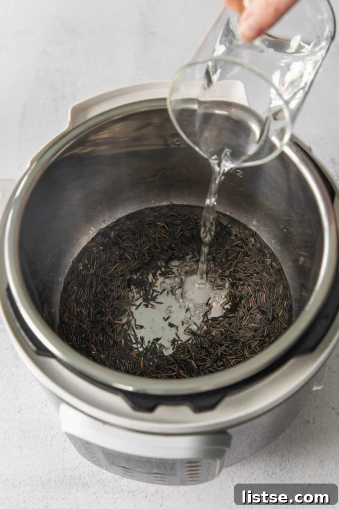 Adding water to an Instant Pot containing wild rice, preparing it for pressure cooking.