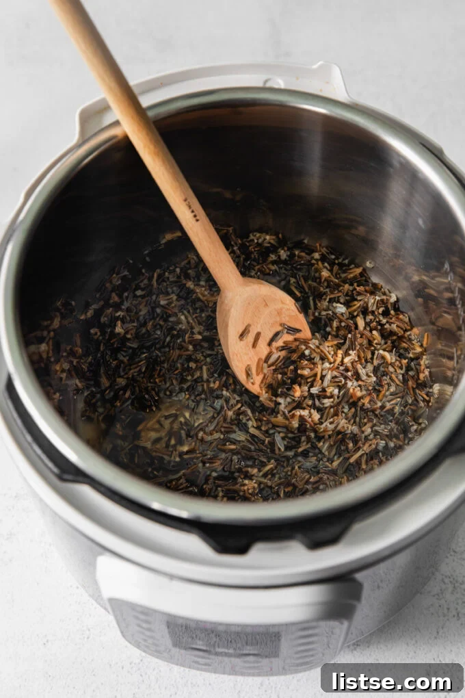 Stirring cooked wild rice in an Instant Pot with a utensil, showing its fluffy texture.
