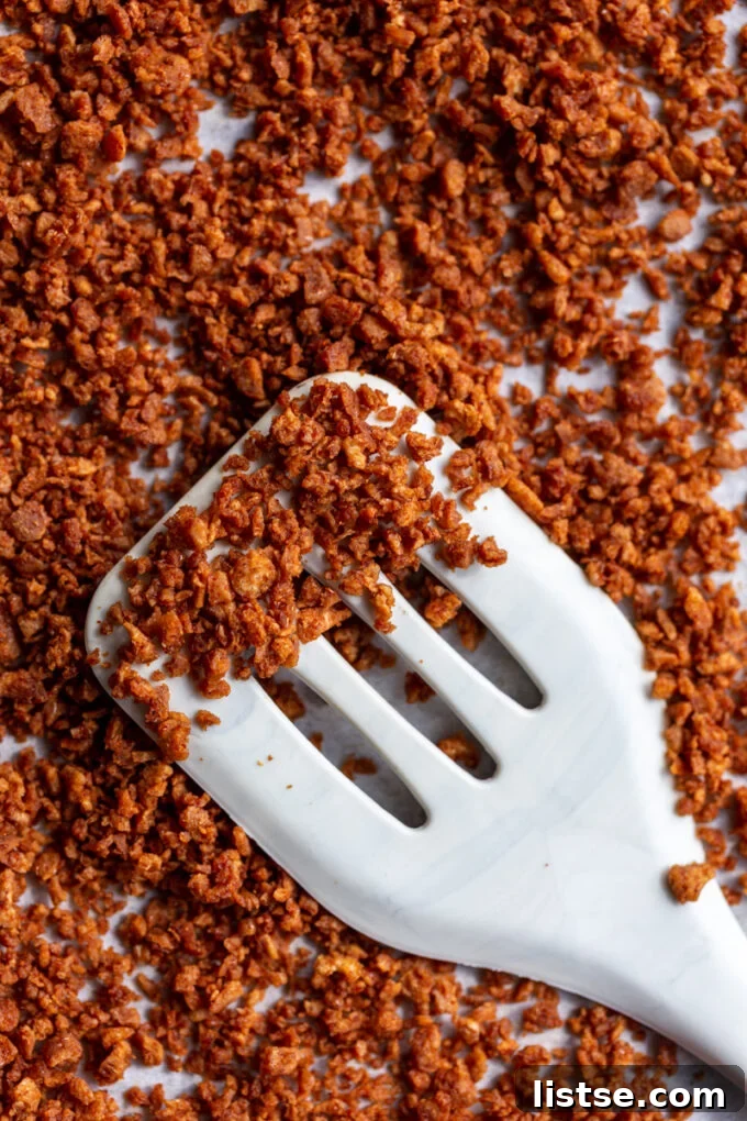Freshly baked vegan bacon bits cooling on a parchment-lined baking sheet, with a spatula lifting some