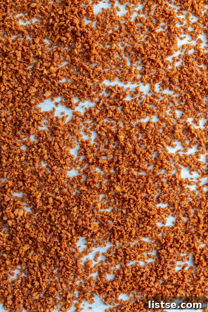 Crispy vegan bacon bits evenly spread on a parchment-lined baking sheet after baking